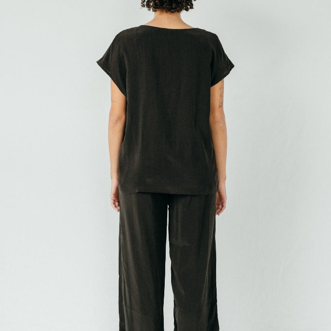 The model stands with her back to the camera and wears the "Noe" blouse and the "Coco" pants