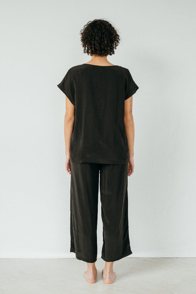 The model stands with her back to the camera and wears the "Noe" blouse and the "Coco" pants