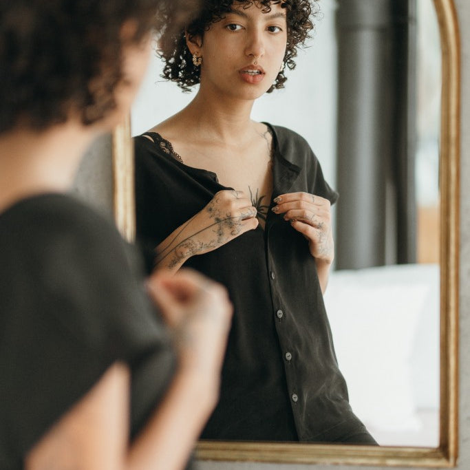 The woman looks at herself in the mirror and buttons the top button of her blouse