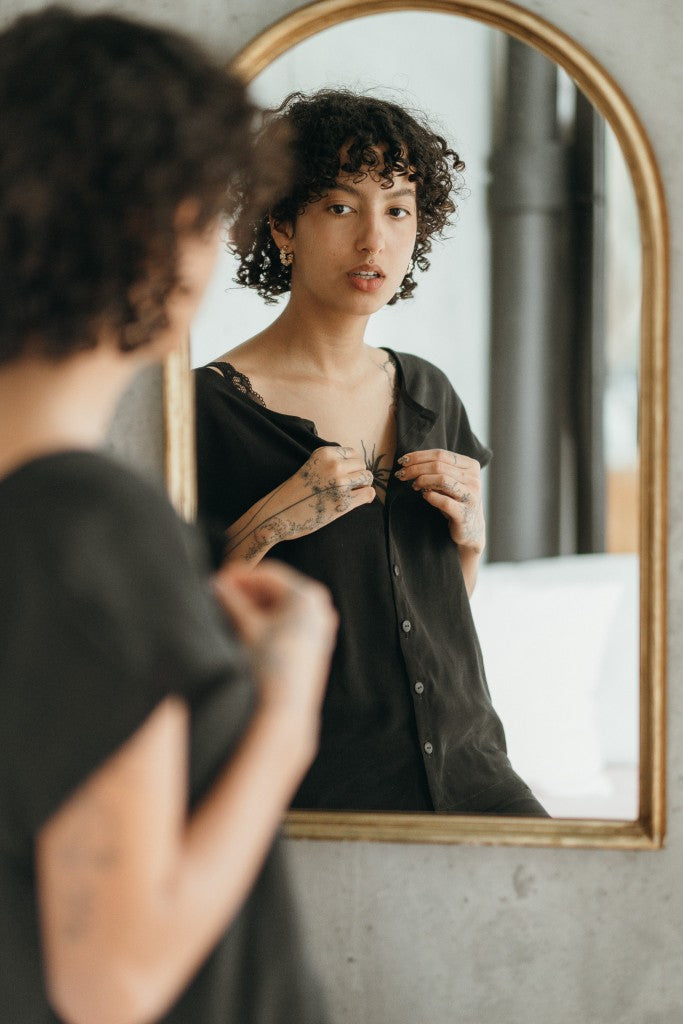 The woman looks at herself in the mirror and buttons the top button of her blouse