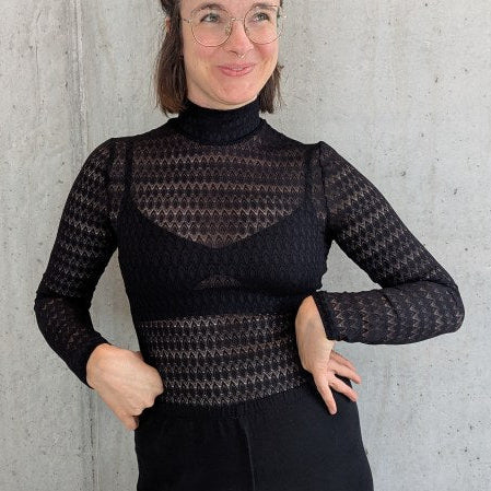 Model trägt den Paula Spitzenpulli, die Arme hat sie in die Hüfte gestemmt und sie blickt in die Luft.