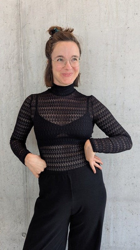 Model trägt den Paula Spitzenpulli, die Arme hat sie in die Hüfte gestemmt und sie blickt in die Luft.