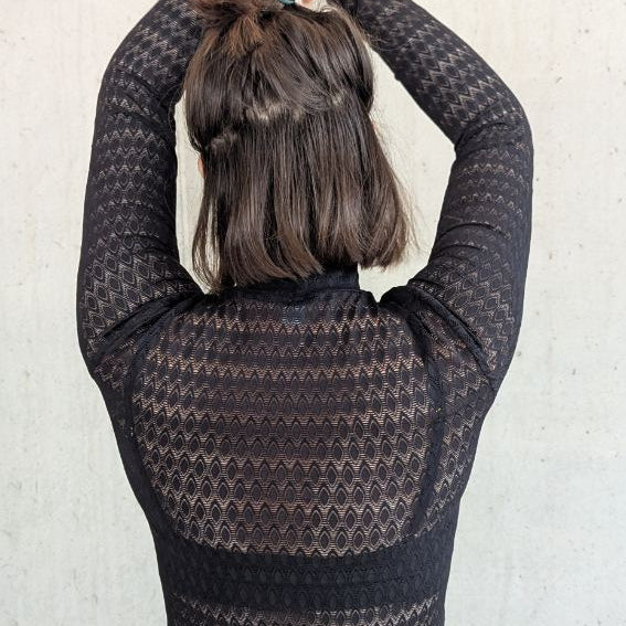 Model trägt den Paula Spitzenpulli. Sie steht mit dem Rücken zur Kamera, die Hände hält sie über den Kopf.
