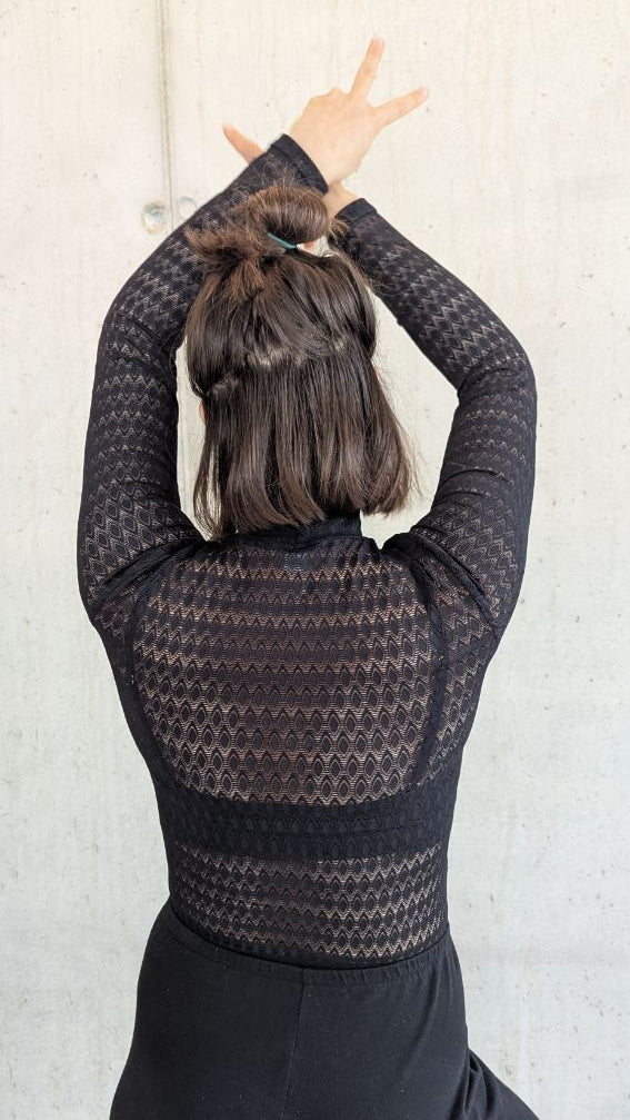 Model trägt den Paula Spitzenpulli. Sie steht mit dem Rücken zur Kamera, die Hände hält sie über den Kopf.