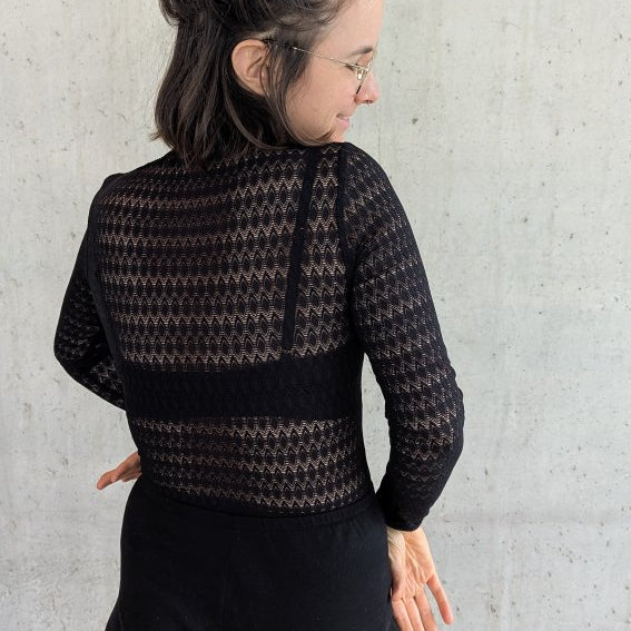 Model trägt den Paula Spitzenpulli und steht mit dem Rücken zur Kamera.