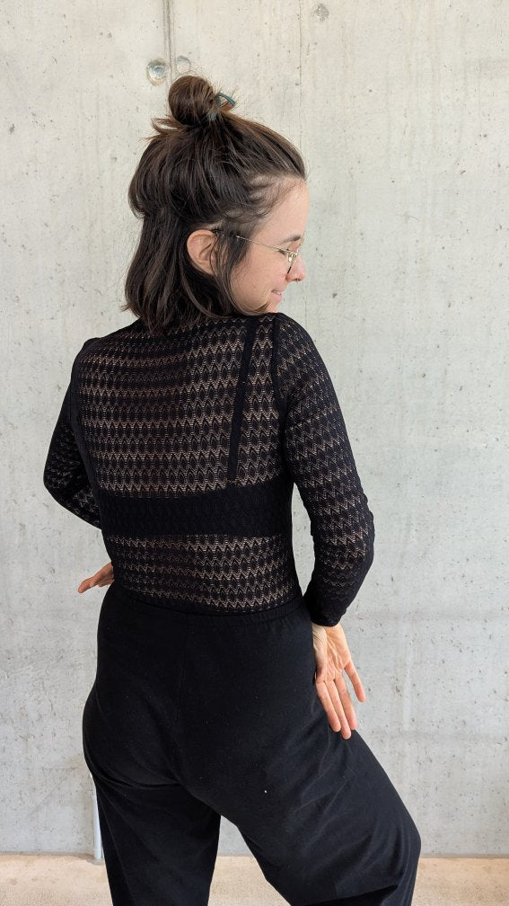 Model trägt den Paula Spitzenpulli und steht mit dem Rücken zur Kamera.