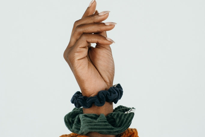 Hand einer Frau, die drei unterschiedliche Scrunchies am Handgelenk trägt.