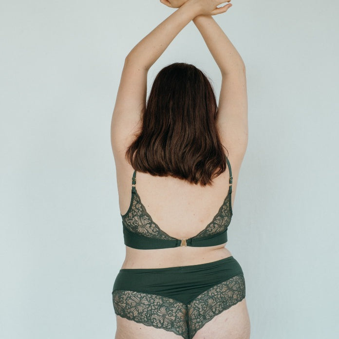 das Model steht zur Wand und hält sich die Hände über den Kopf und posiert in schöner Unterwäsche