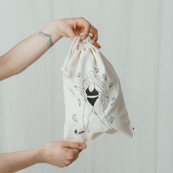Hands holding wash bag with illustration of dancing woman in underwear.