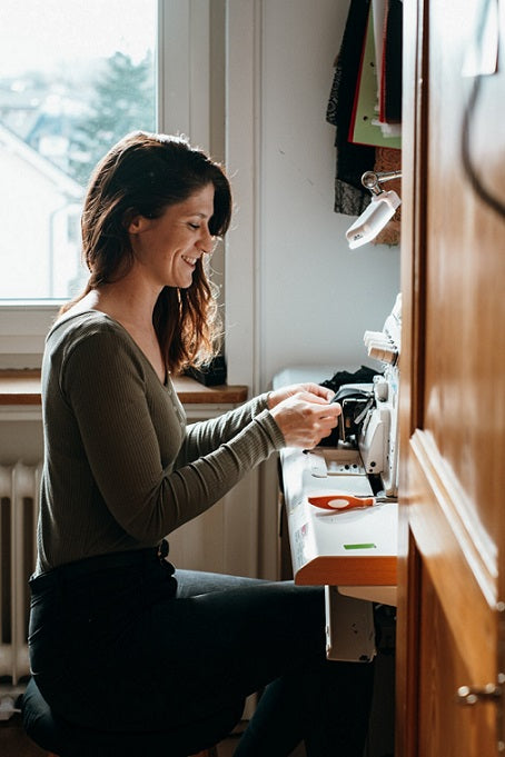 Foto zeigt Kira an der Overlock Nähmaschine. Sie näht gerade einen Slip.
