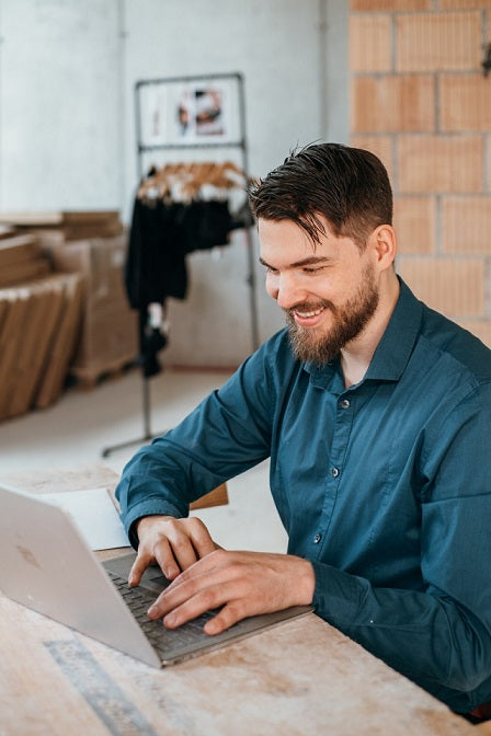 Foto zeigt Aaron. Er sitzt mit dem Laptop am Tisch.