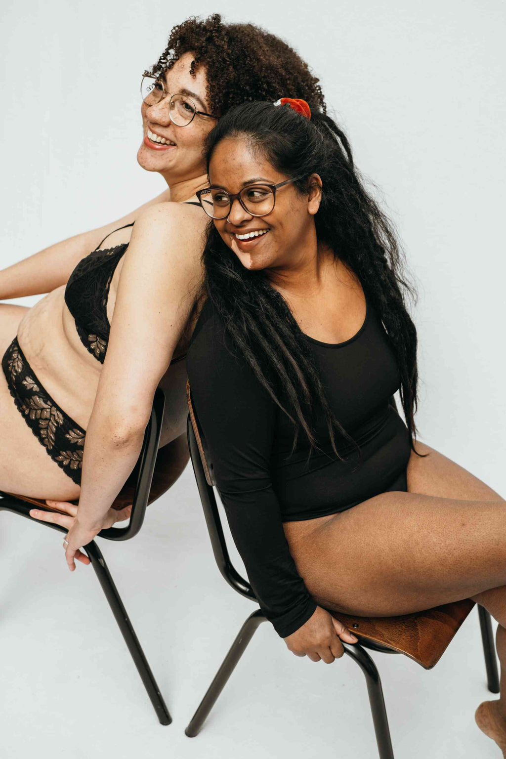 Foto zeigt zwei unserer Models, sie sitzen Rücken an Rücken und lachen gemeinsam.