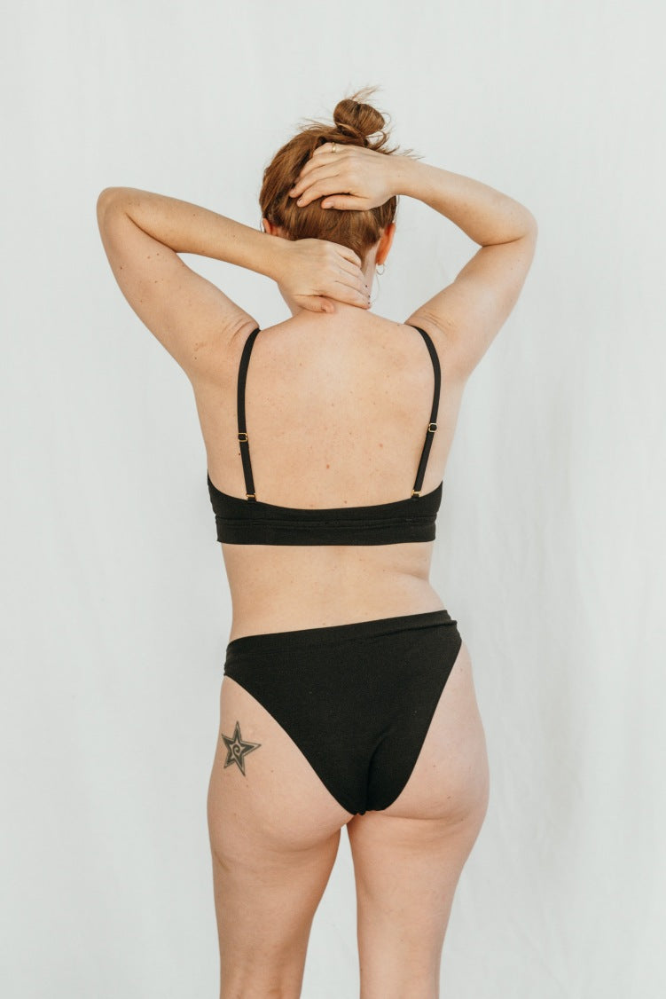 Woman wears sustainable bra and plain underpants in black.