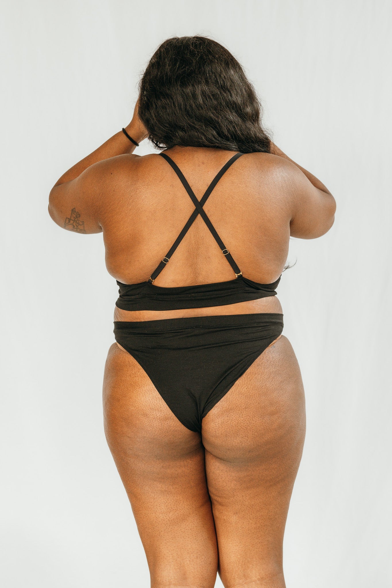Person wears bra with crossed straps and high waist slip in black.