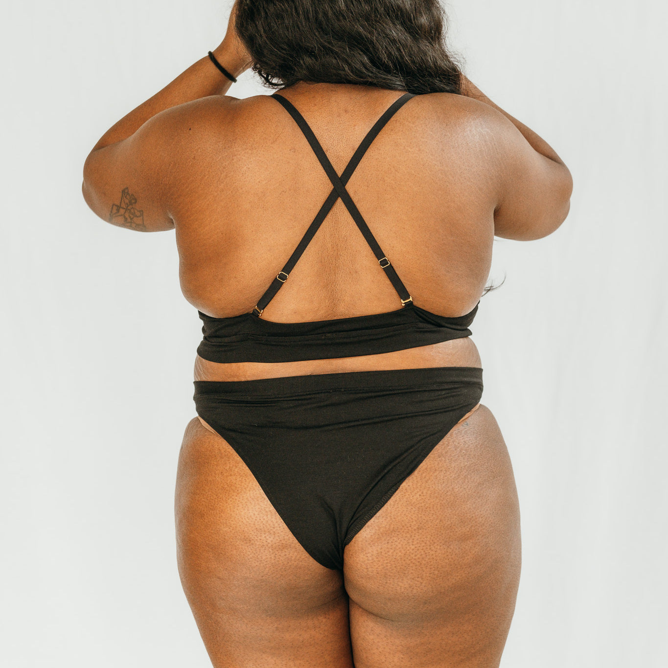 Person trägt BH mit gekreuzten Trägern und High Waist Slip in schwarz.