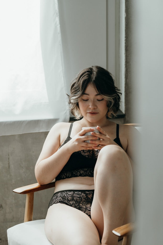 Person in black romantically playful Bralette drinks coffee.