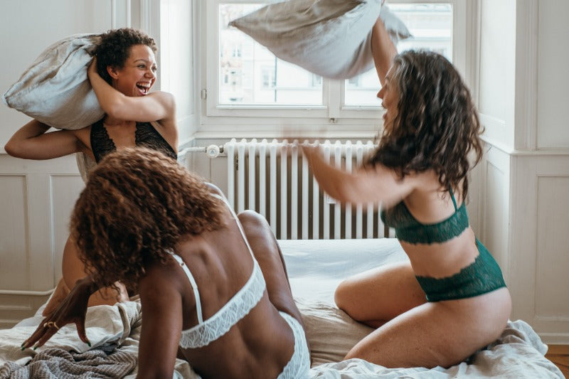 drei Frauen machen in Unterwäsche auf dem Bett eine Kissenschlacht.