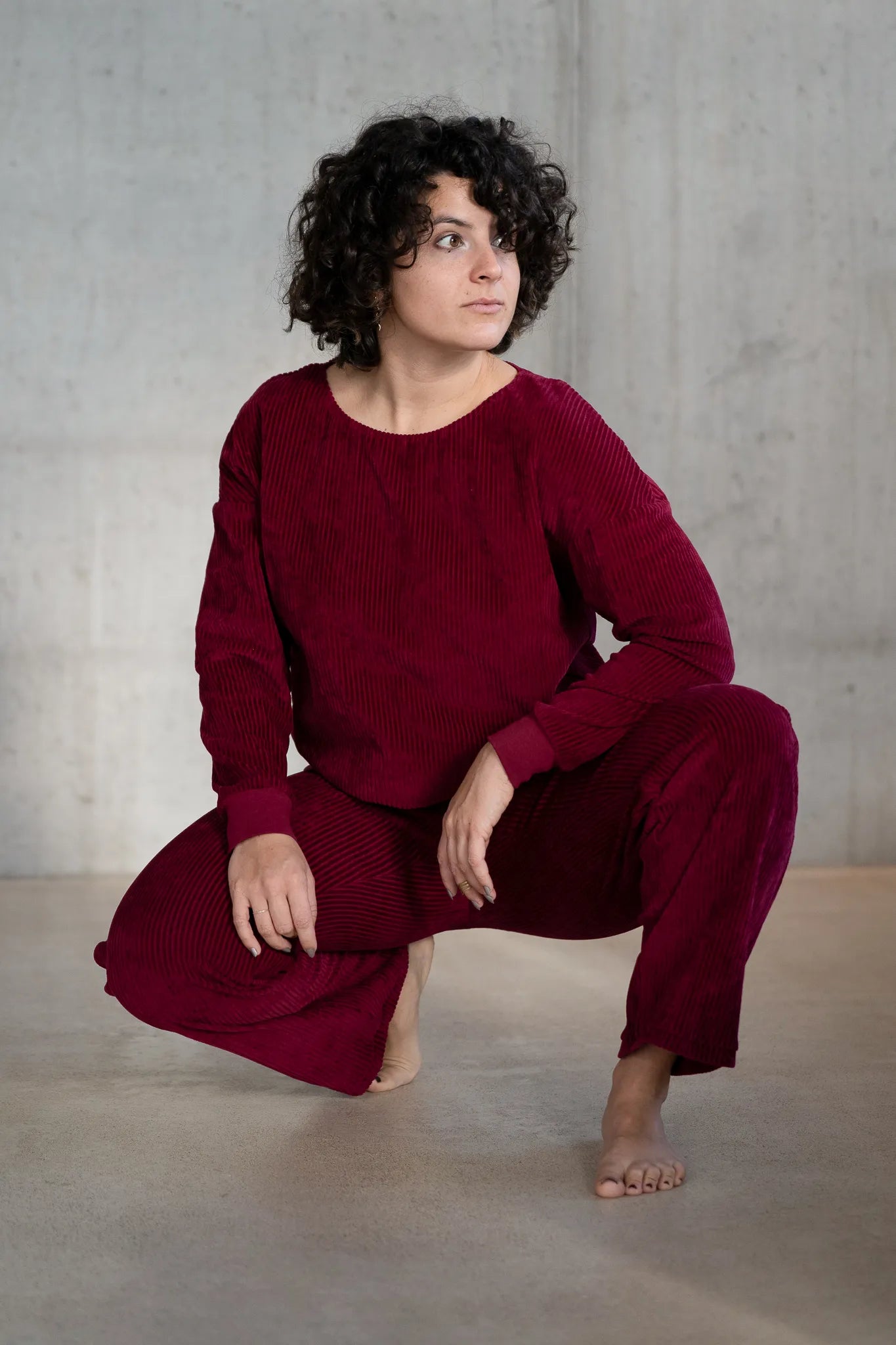 Model ist in einer tiefen Hocke und trägt den Chloé Pulli und die Kelly Hose in Ruby Red.