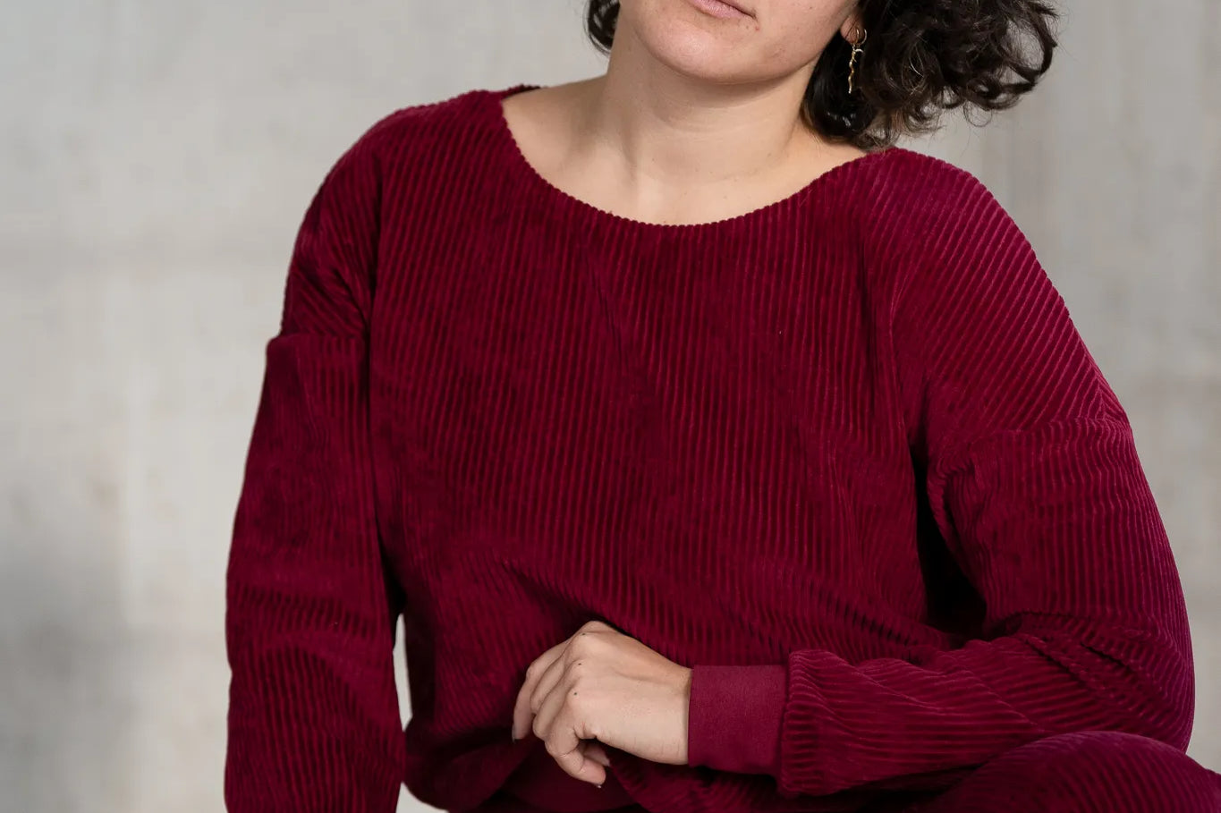 Model kniet am Boden, sie trägt den Chloé Pullover und die Fiona Hose in Ruby Red und blickt direkt in die Kamera. Ein Bein hat sie aufgestellt.