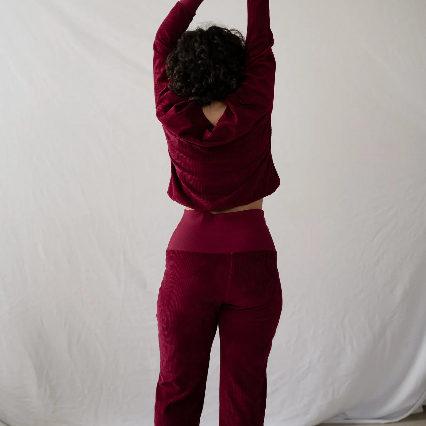 Model steht mit dem Rücken zur Kamera, die Hände hat sie in die Luft gestreckt. Sie trägt den Chloé Pullover und die Fiona Hose in Ruby Red.