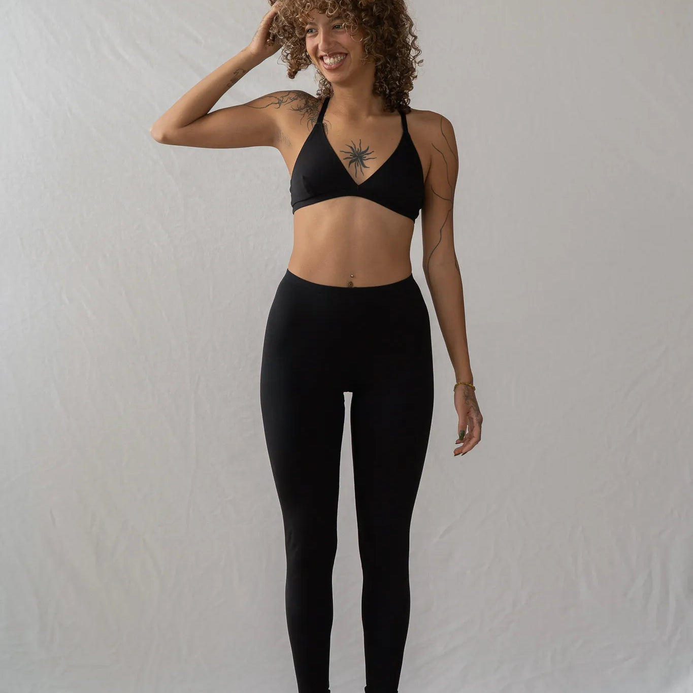 Model steht vor einem weissen Hintergrund auf den Zehenspitzen und lächelt. Sie trägt die Inge Leggins und das Dina Bralette.