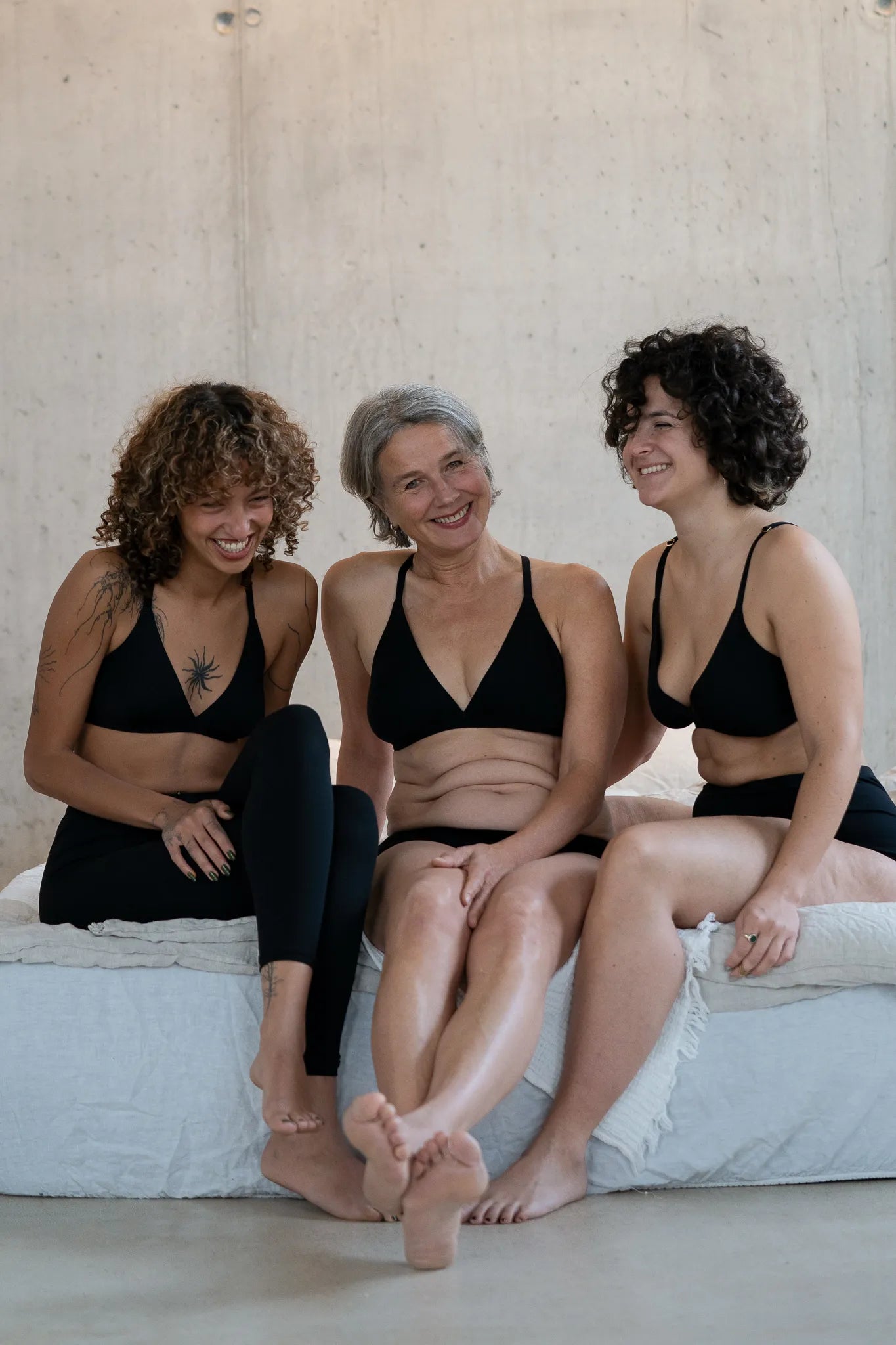 Drei Models sitzen nebeneinander auf der Bettkante und lachen zusammen. Sie tragen unsere neue Cotton Collection.