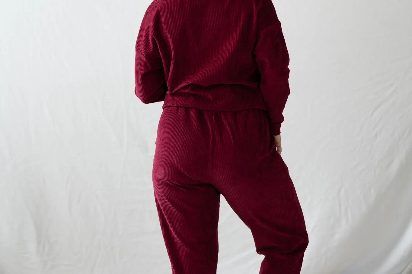 Model steht mit dem Rücken zur Kamera gerichtet, den Kopf leicht zur Seite gelegt. Sie trägt den Chloé Pulli und die Kelly Hose in Ruby Red.