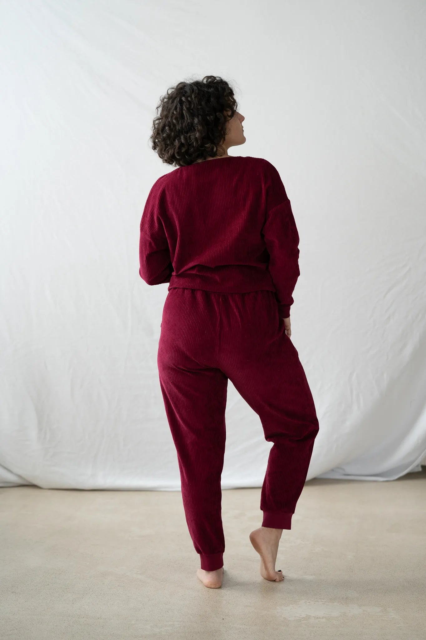 Model steht mit dem Rücken zur Kamera gerichtet, den Kopf leicht zur Seite gelegt. Sie trägt den Chloé Pulli und die Kelly Hose in Ruby Red.