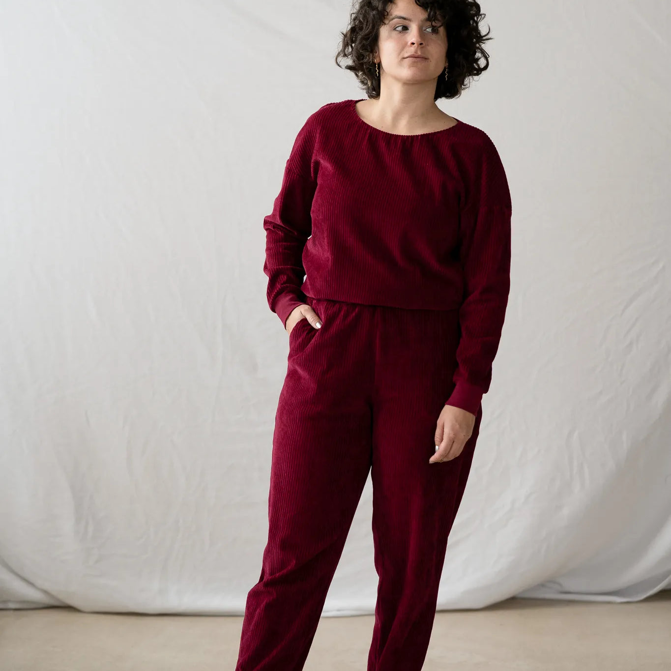 Model steht in der Fiona Hose und dem Chloé Pullover in Ruby Red vor weissem Hintergrund. Die rechte Hand hat sie lässig in der Hosentasche.