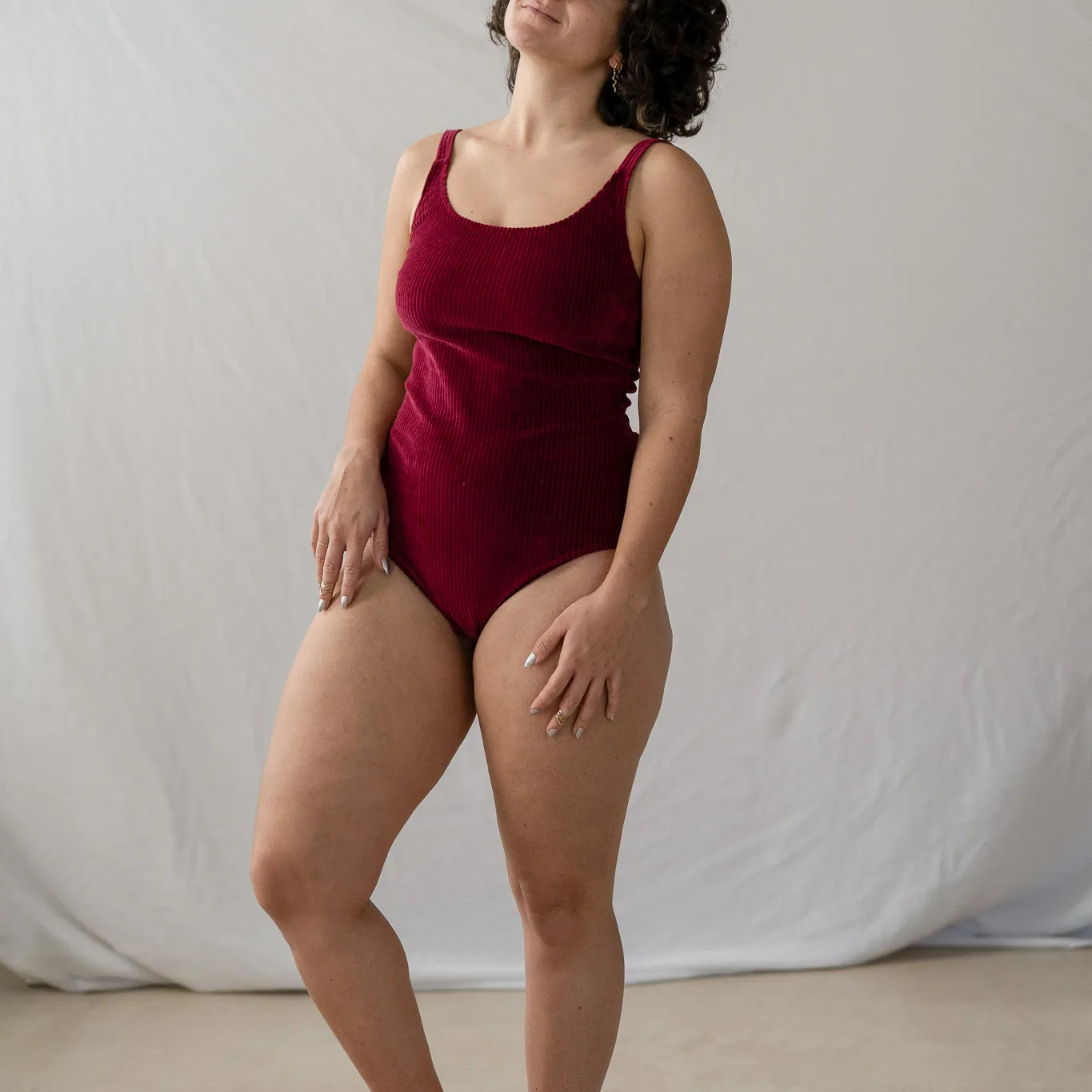 Model steht im roten Ronja Body vor weissem Hintergrund, den Kopf hat sie leicht seitwärts geneigt und sieht verträumt in die Luft.