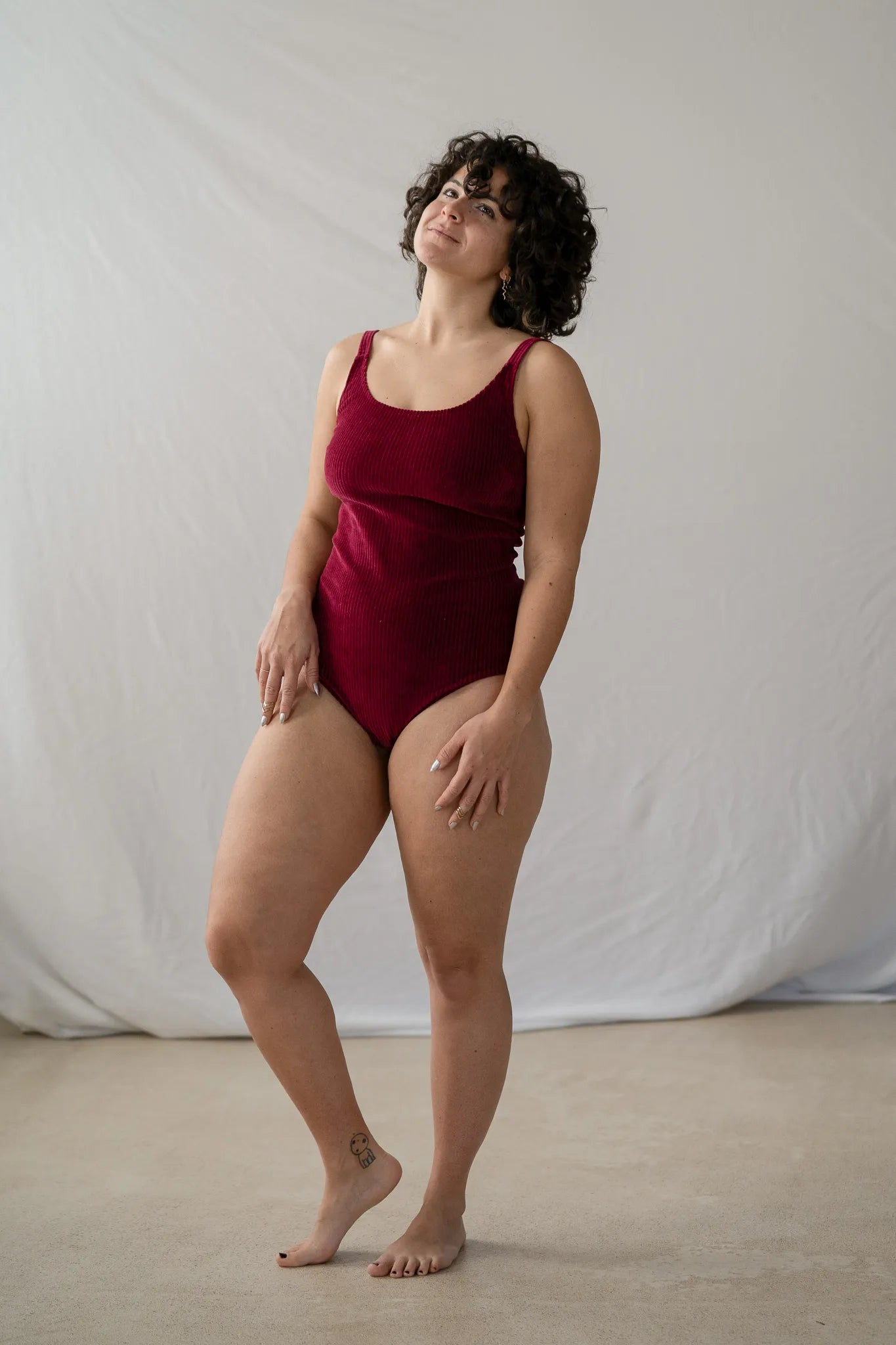 Model steht im roten Ronja Body vor weissem Hintergrund, den Kopf hat sie leicht seitwärts geneigt und sieht verträumt in die Luft.