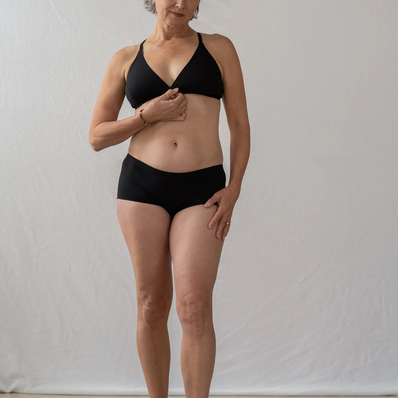 Model steht vor einem weissen Vorhang und sieht direkt in die Kamera. Sie trägt das Dina Bralette und die Wilma Panty.