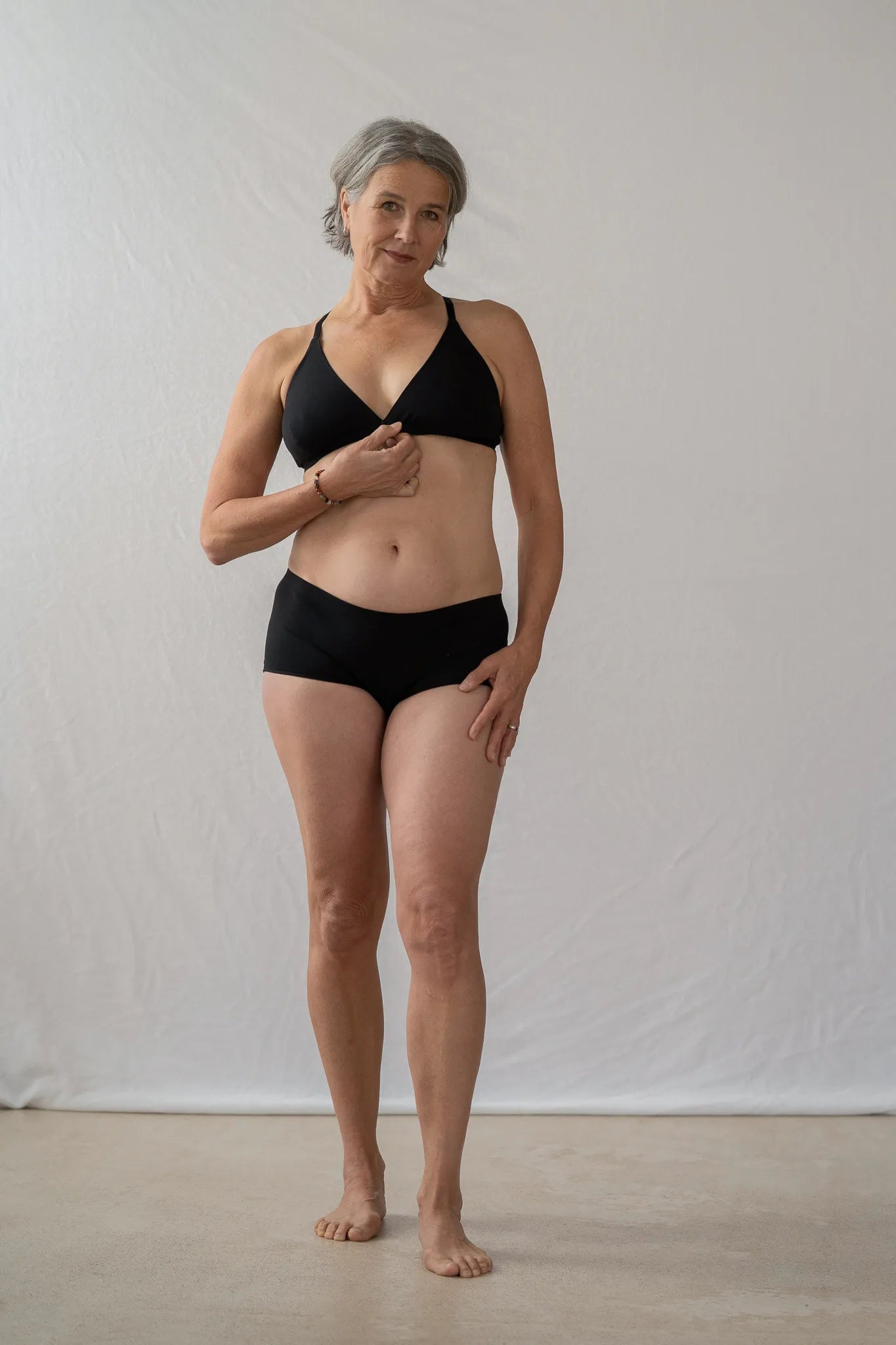 Model steht vor einem weissen Vorhang und sieht direkt in die Kamera. Sie trägt das Dina Bralette und die Wilma Panty.