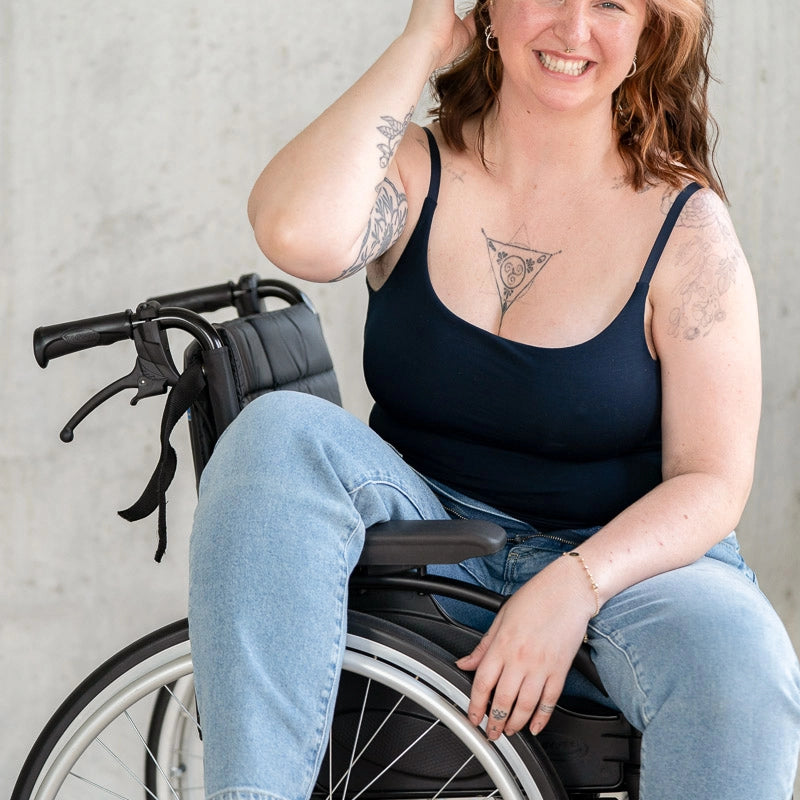 Model sitzt im Rollstuhl und lacht in die Kamera. Sie trägt das Carla Camitop in Night Blue und dazu eine Jeanshose.
