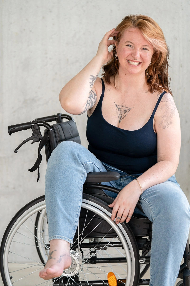 Model sitzt im Rollstuhl und lacht in die Kamera. Sie trägt das Carla Camitop in Night Blue und dazu eine Jeanshose.