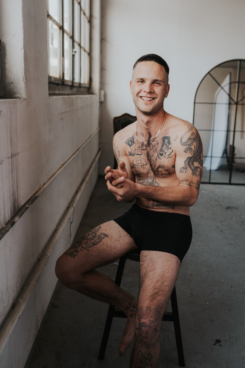 Menn sits on high chair and laughs into the camera. He is wearing black underpants made of TENCEL™. 