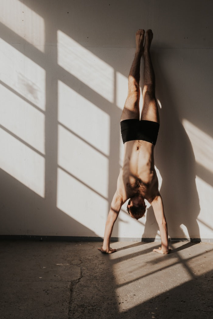 Person does handstand on the wall in boxer shorts.