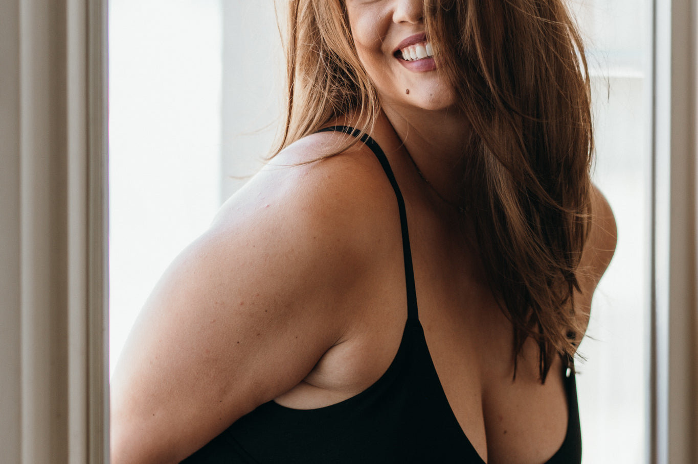 Model schwingt die Haare und lächelt. Sie trägt Basic Bralette und Unterhose aus TENCEL™