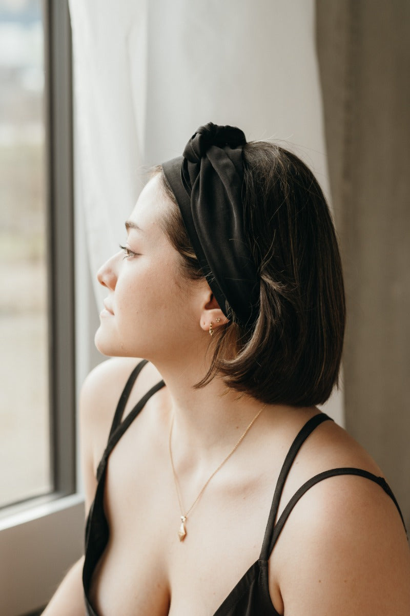 Frau schaut aus dem Fenster und trägt ein schwarzes Haarband.