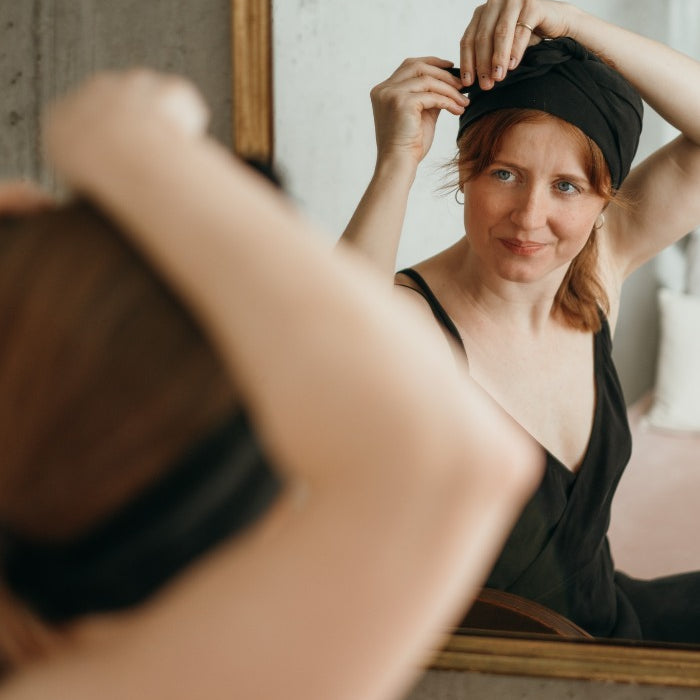 Woman in a black negligee ties a hairband in her hair with concentration.