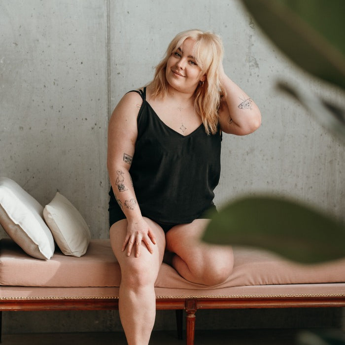 Woman sitting on rose sofa with pillows and wearing black short pajamas.