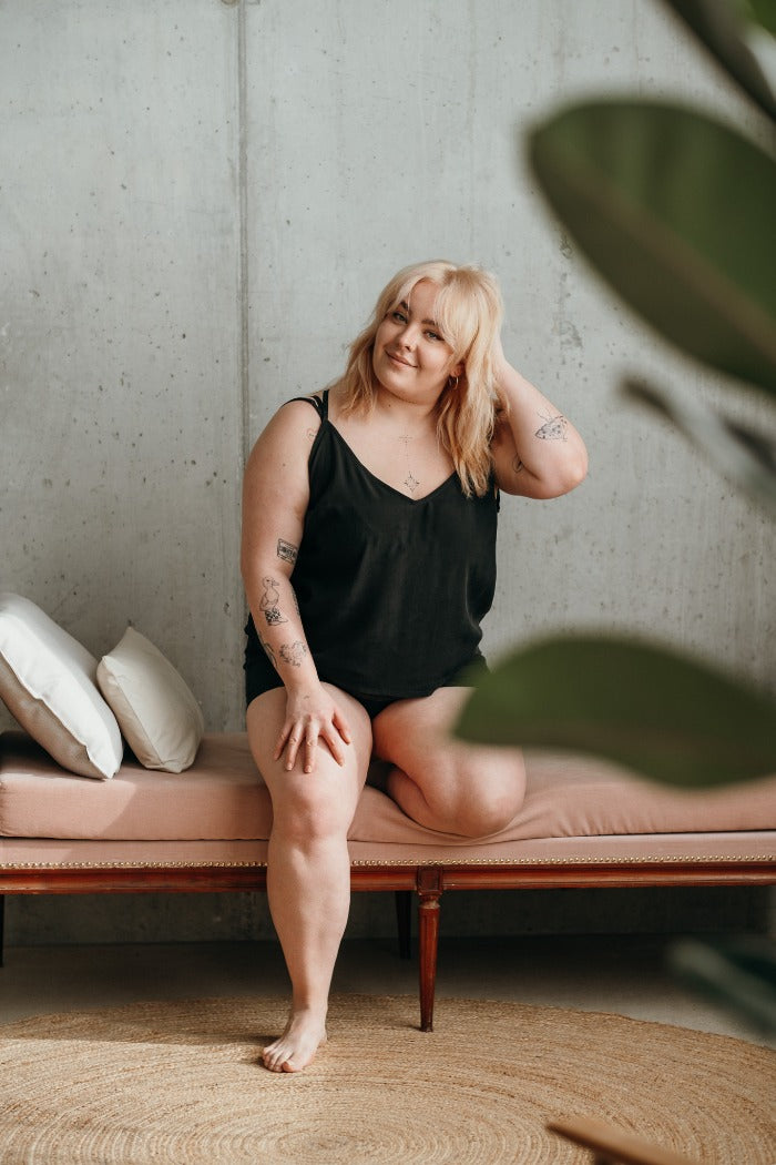 Woman sitting on rose sofa with pillows and wearing black short pajamas.