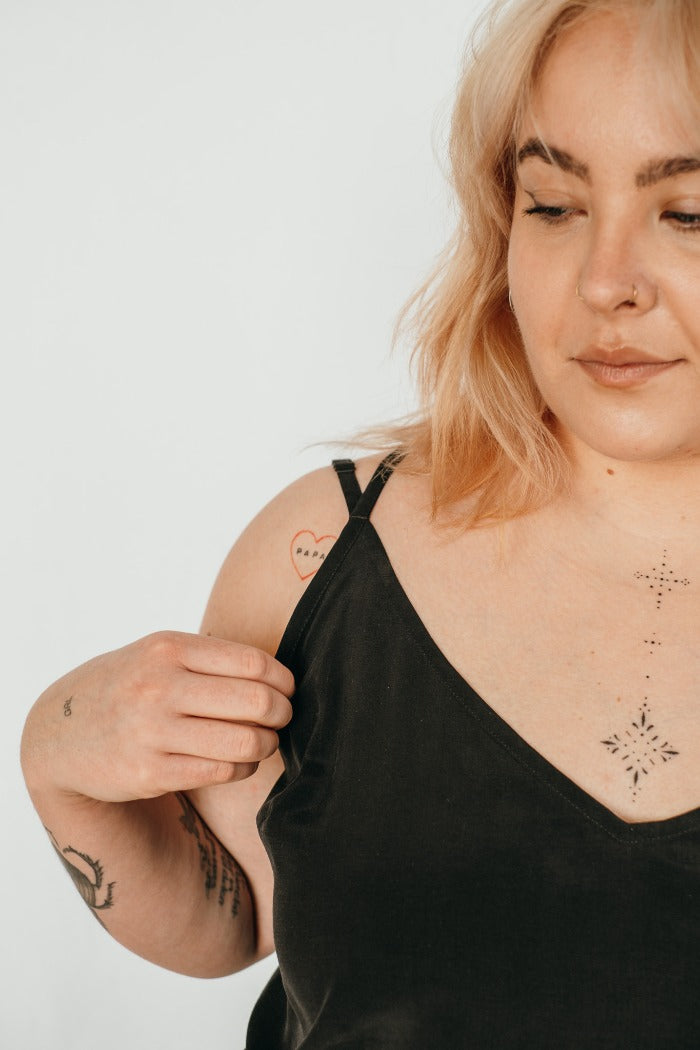 Une femme avec des tatouages porte un haut avec de fines bretelles.