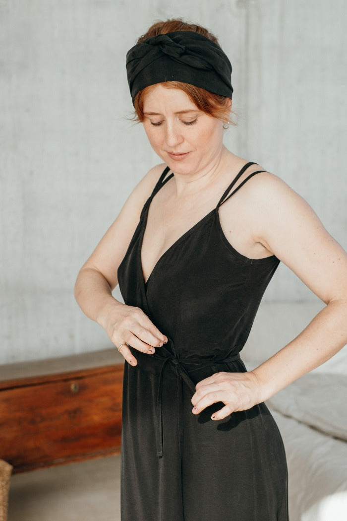 Frau bindet konzentriert das schwarze Wickelkleid aus seidigem Cupro.