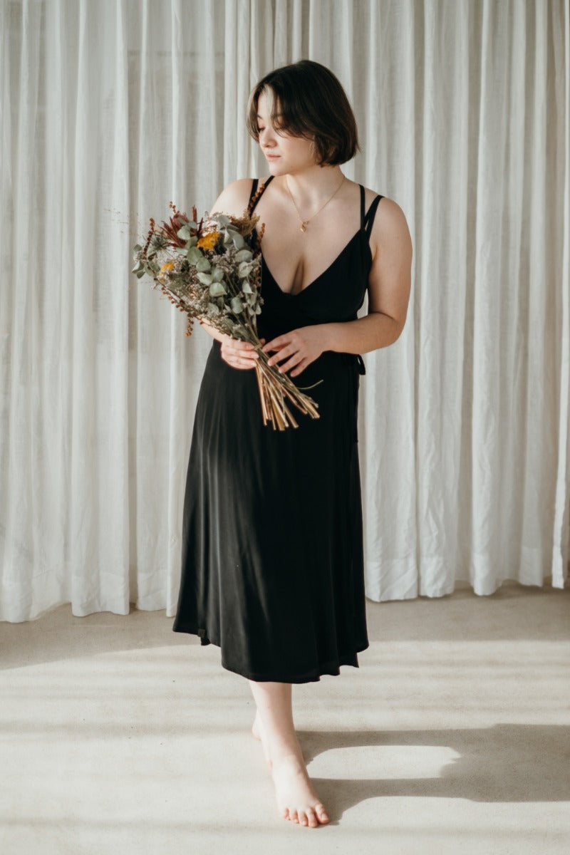 Woman wearing wrap dress by thoughts of september and holds bouquet of flowers.