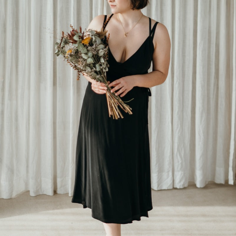 Woman wearing wrap dress by thoughts of september and holds bouquet of flowers.