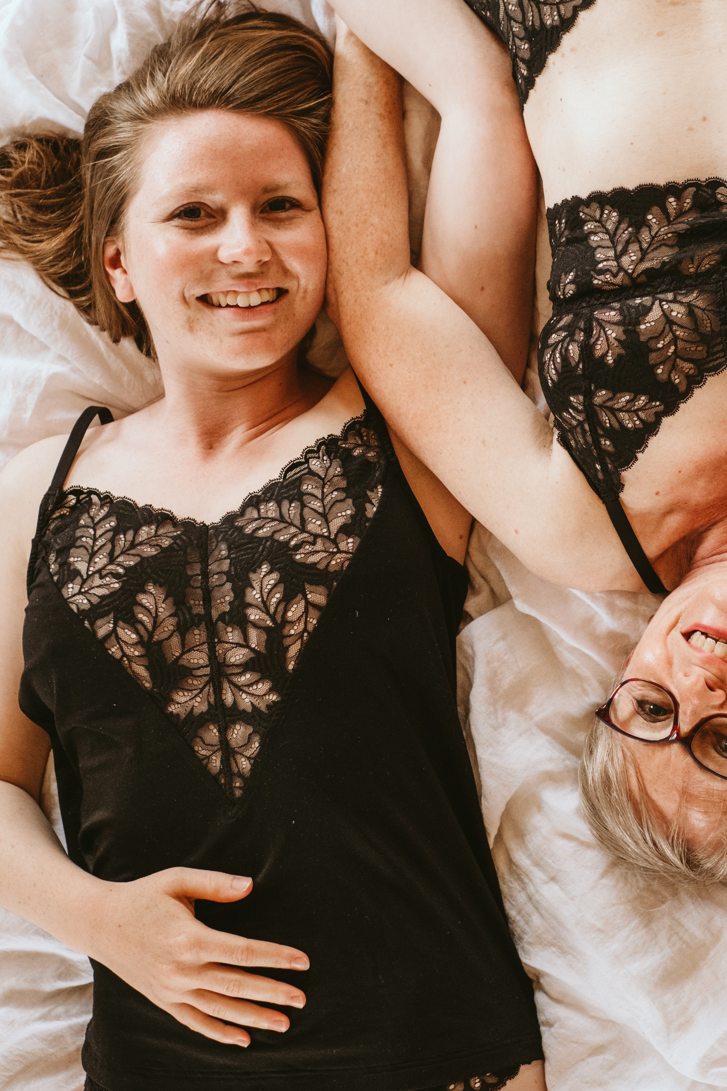 Mother and daughter are lying together on the bed, both are wearing black underwear.