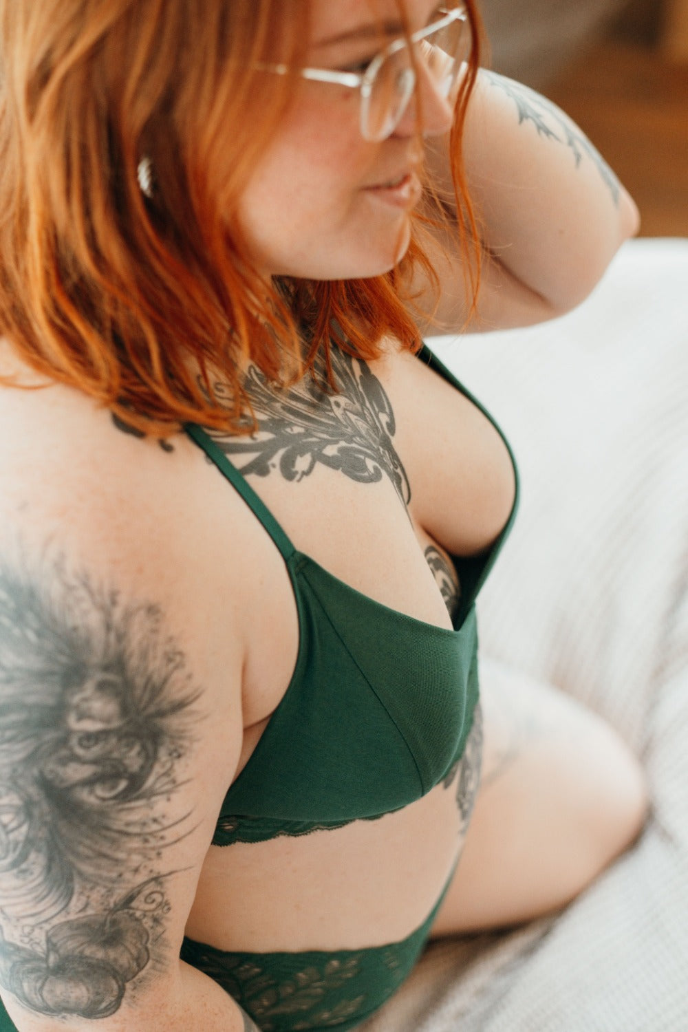 Donna inginocchiata sul letto con indosso biancheria di pizzo verde scuro e TENCEL.