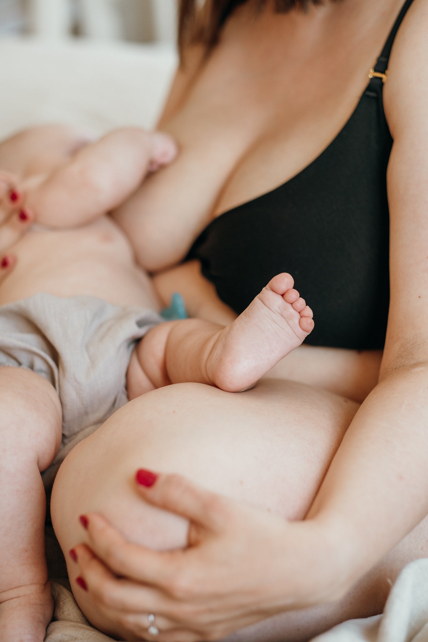 Donna seduta sul letto che allatta il suo bambino, indossando un reggiseno nero per l'allattamento