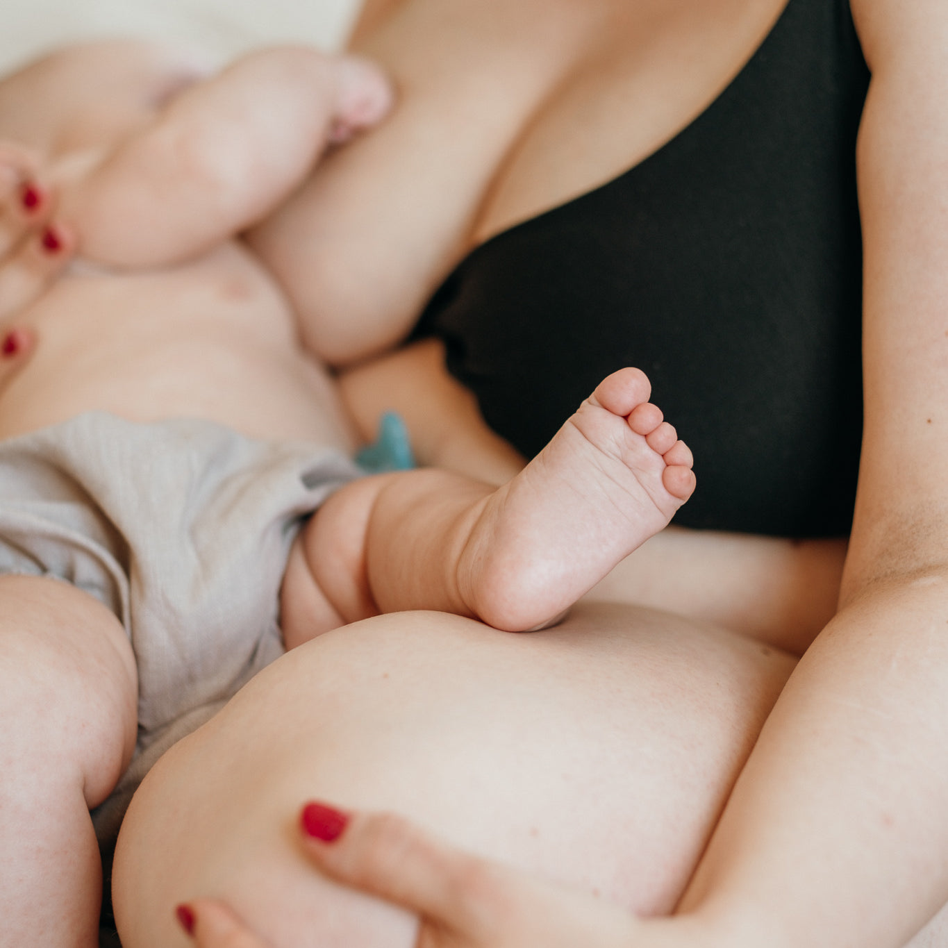 Woman sitting on bed breastfeeding her baby wearing black nursing bra